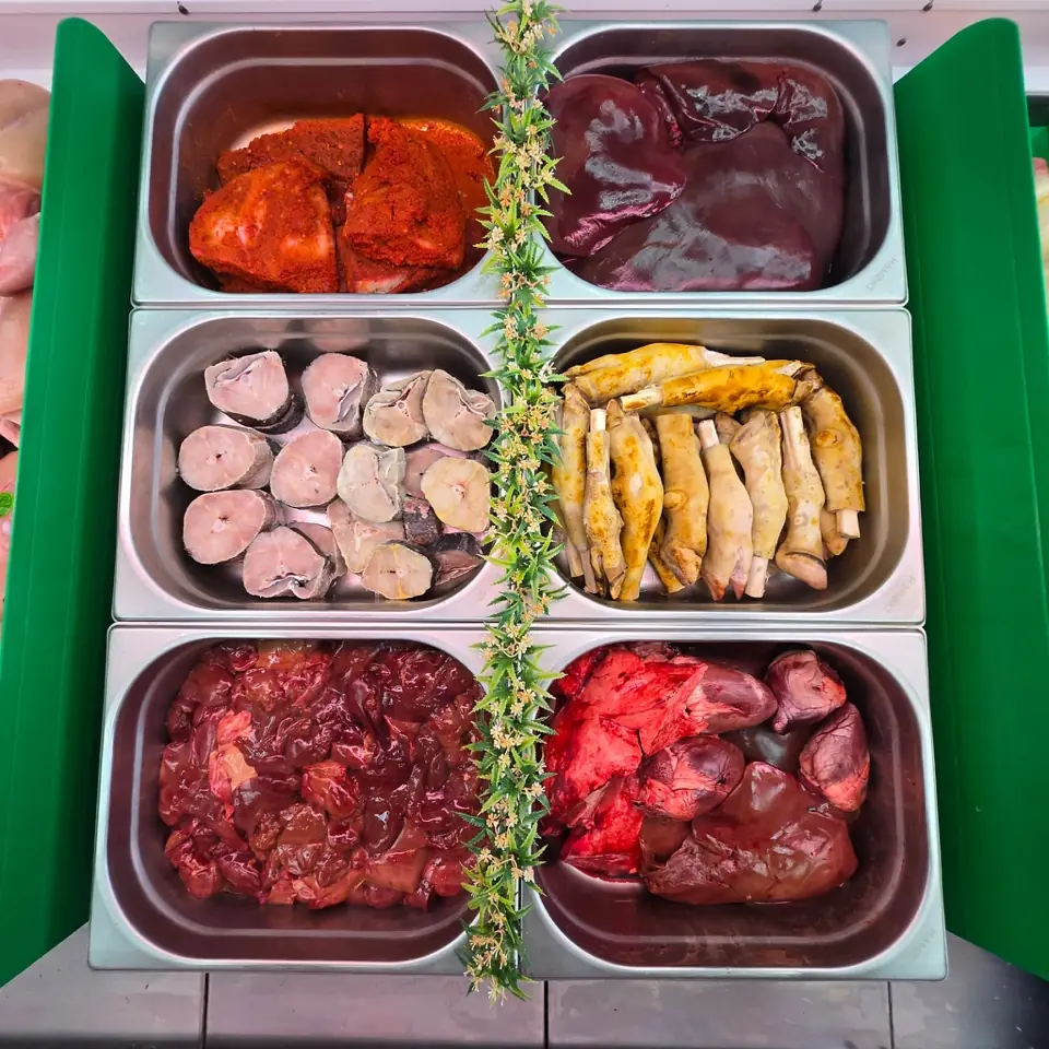 Steel trays at the counter: marinated pieces, liver, fish steaks, chicken feet and offal